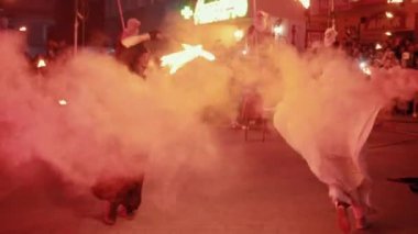 Adam alevlerle kıvranıyor, kadın etrafını dumanla sararak erkeğin etrafında koşuyor.