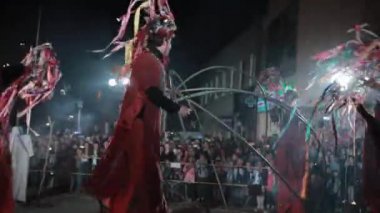 Kırmızı kostümlü Stilt Walker 'lar, süslü şapkalı çelenklerle dans edenler..