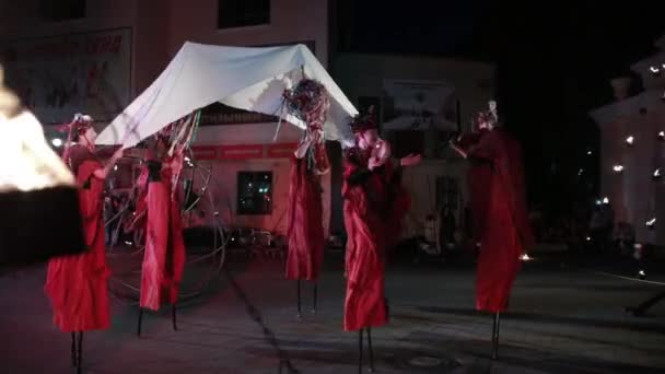 Stilt walkers in costumi rossi tenere tessuto bianco sulla cima di bastoni . — Video Stock