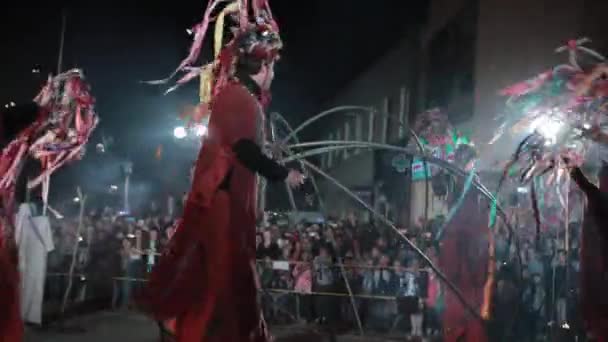 Stilt walkers in costumi rossi, cappelli decorati danzano con ghirlande . — Video Stock