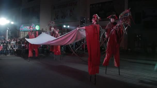 Stilt walker dengan kostum merah, topi dihiasi menari dengan sepotong kain . — Stok Video