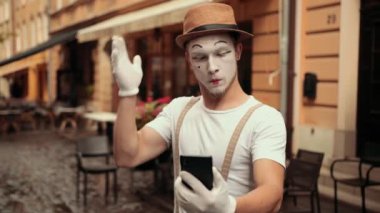 Genç yakışıklı pandomimci telefona bakıyor, şaşırmış, kafası karışmış..