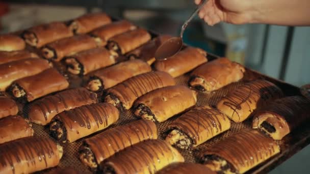 Köchin weibliche Hand gießt dunkle geschmolzene Schokolade auf Brötchen mit Mohn. — Stockvideo