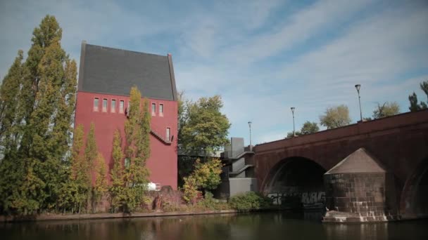 Hermosa casa alta roja en el lado opuesto del río, un antiguo puente sobre el estanque . — Vídeo de stock