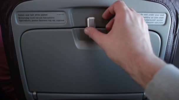 Male hand is unlocking personal food tray located on seat before him. — Stock Video