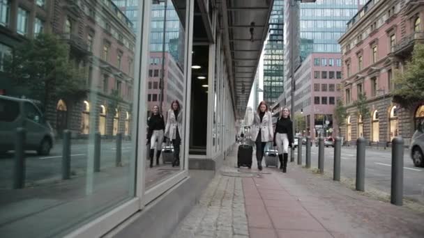 Twee mooie meisjes lopen met koffers op de stoep in de buurt van glazen gebouw. — Stockvideo