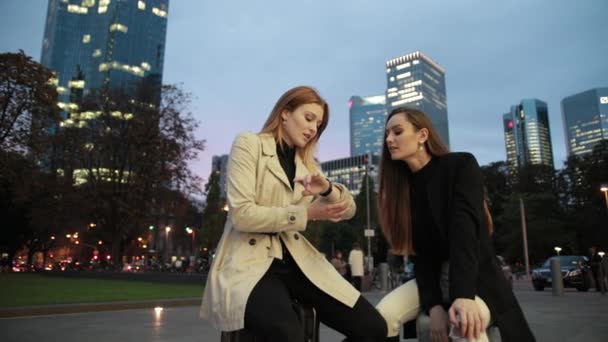 Deux jeunes jolies filles sont assises sur des valises dans le parc de la ville le soir . — Video