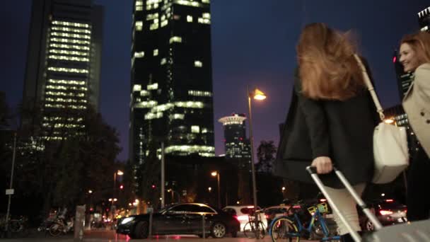 Dos mujeres jóvenes atractivas están rodando sus maletas por la noche en la calle . — Vídeos de Stock
