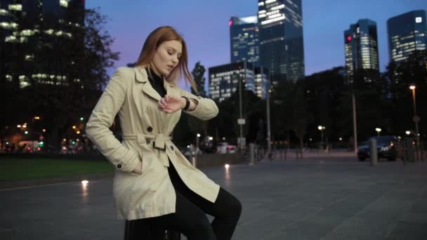 En attraktiv rødhåret pige venter på nogen, der sidder på kufferten . – Stock-video