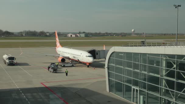 Blick aus dem Flughafenfenster auf Terminal, Flugzeug mit Düsenbrücke, Fahrzeuge. — Stockvideo