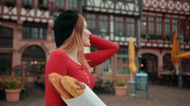 Французская девушка в черном берете держит в руках завернутые в бумагу хлебы улыбается , — стоковое видео