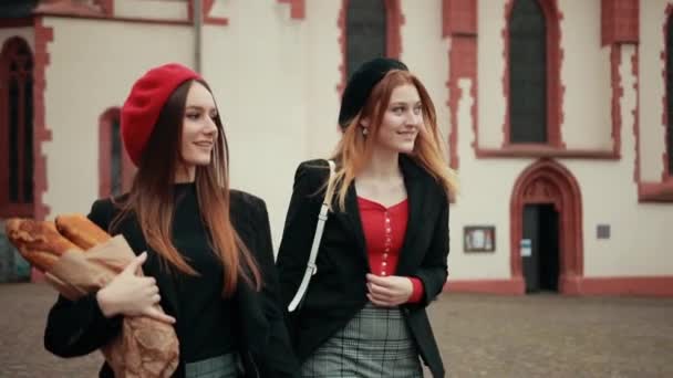 Дві французькі дівчини в чорних куртках і берети йдуть по вулиці, тримаючись за руки. — стокове відео