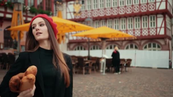 Французька молода жінка, одягнена в чорну куртку, тримаючи паперу загорнутий хліб під рукою. — стокове відео