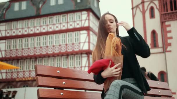 Γαλλίδα με μαύρο σακάκι κάθεται κρατώντας μακριά καρβέλια ψωμί τυλιγμένα σε χαρτί — Αρχείο Βίντεο