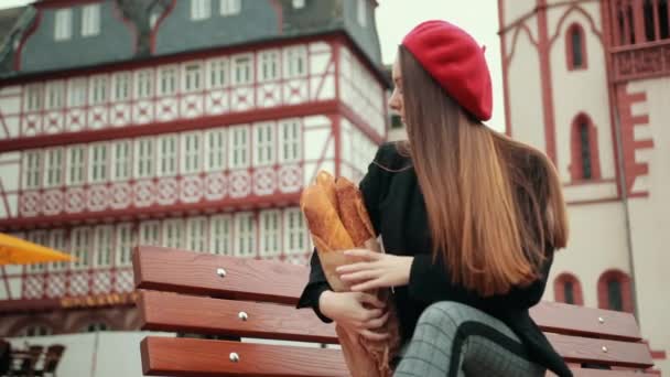 Französin sitzt in schwarzer Jacke auf Bank und hält Brotlaibe — Stockvideo