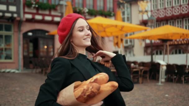 法国女人，身穿黑色夹克，头戴红色贝雷帽，拿着纸包的面包 — 图库视频影像