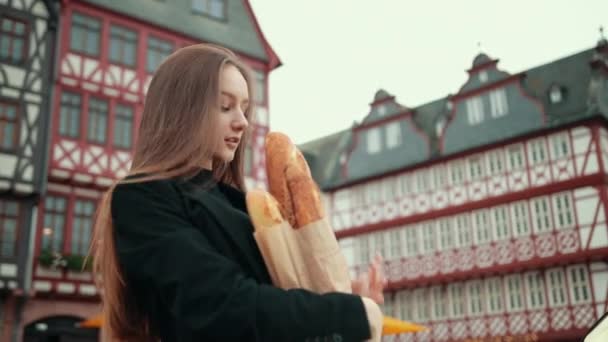 Duits meisje in zwart jasje onhandig houdt papier verpakt broden onder haar hand, — Stockvideo