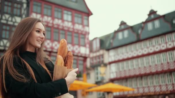 Mooi duits meisje in zwart jasje onhandig houdt papier verpakt broden hand — Stockvideo