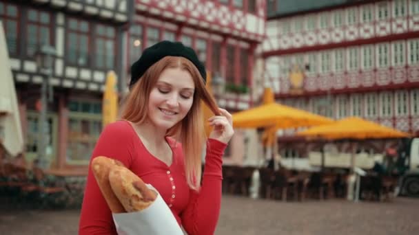 Французская девушка в черном берете держит завернутые в бумагу хлебы и показывает большой палец вверх . — стоковое видео