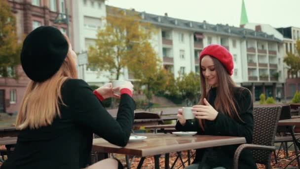 Two beautiful seductive women French sit on the street and drink coffee — Stock Video