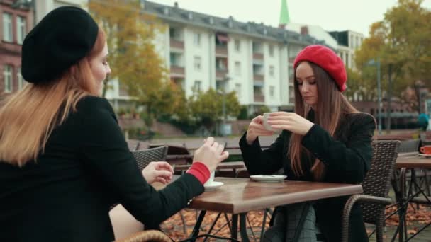 Dos hermosas mujeres seductoras francesas se sientan en la calle y beben café — Vídeos de Stock