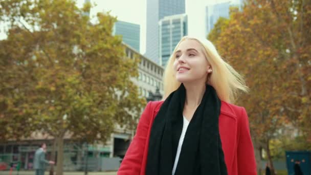 Blond meisje op de achtergrond van de moderne stad gaat voorwaarts bochten in de voorkant van de camera — Stockvideo
