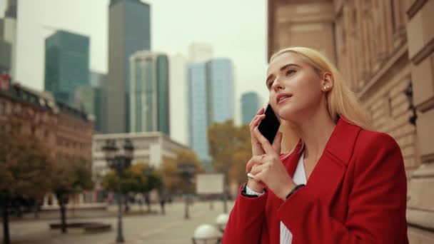 Mulher loira está falando ao telefone contra o pano de fundo da metrópole moderna — Vídeo de Stock