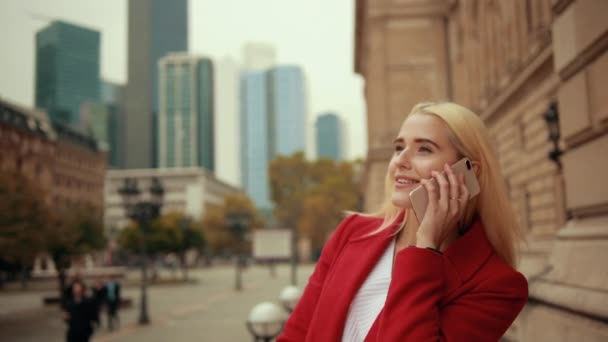 Blond kvinna talar i telefon mot bakgrund av modern metropol — Stockvideo