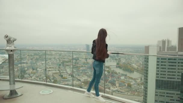 Mujer bonita se encuentra en la partición transparente y admira el paisaje urbano — Vídeo de stock