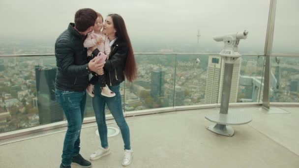 Los padres sostienen a un niño en sus brazos y muestran dibujos animados en su teléfono inteligente . — Vídeo de stock