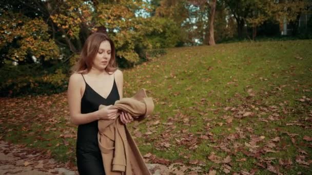 Femme marche à travers un parc d'automne, est froid met manteau brun sur le corps pour garder au chaud — Video