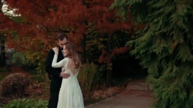Yeni evliler kucaklaşır yeşil kırmızı ağaçların arasında.