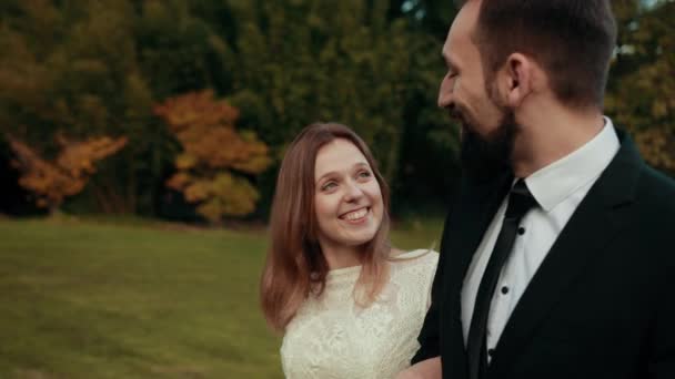 Groom avec barbe marche à travers la pelouse et parle à sa mariée en se souriant . — Video