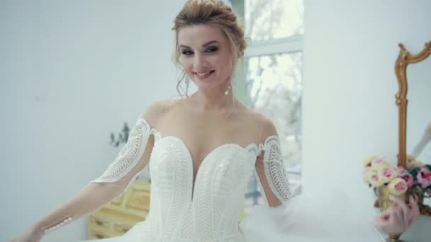 Jong blond bruid in wit jurk is glimlachen poseren voor camera draaien rond. — Stockvideo