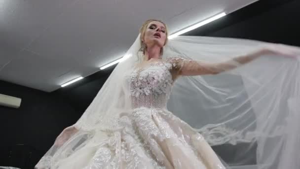 Bride in white wedding dress with crown on head holds veil in hands spreads it, — ストック動画