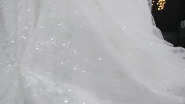 Close-up of white shiny wedding dress, which bride turns left to right.