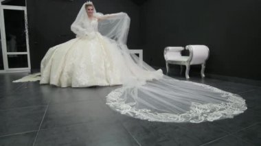 Young beautiful bride in white wedding dress plays with veil pushes it towards
