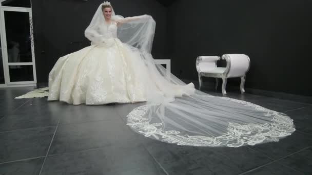 Young beautiful bride in white wedding dress plays with veil pushes it towards — Stock Video