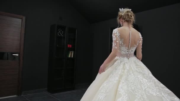 Young blonde bride in white wedding dress with crown poses for camera in room — Stockvideo