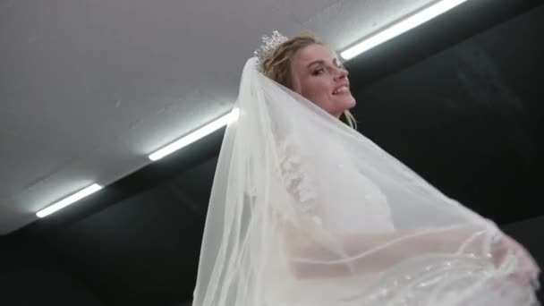 Bride in white wedding dress with crown on head holds veil in hands spreads it — ストック動画