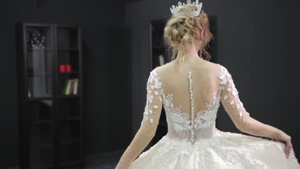 Blonde bride in white wedding dress with crown on head walking forward in room — Stockvideo