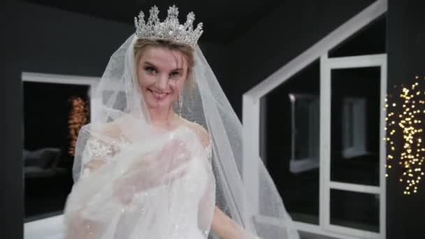 Bride with crown on her head makes minute with hands on veil smiling at camera — Stok video