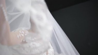 bride in white wedding dress plays with veil throws it at camera in black room