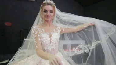 Young bride in white wedding dress sits on bed plays with veil throws it