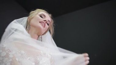 Young bride in white wedding dress plays with veil making waves smiling camera