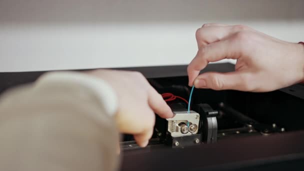 3d technologie twee mannen handen duwen plastic grijze draad in tanden van de printer — Stockvideo