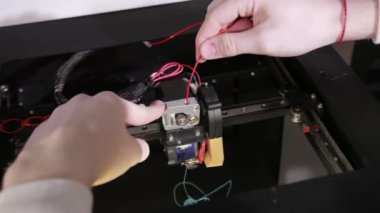 3D technology two mens hands push plastic gray thread into prongs of printer