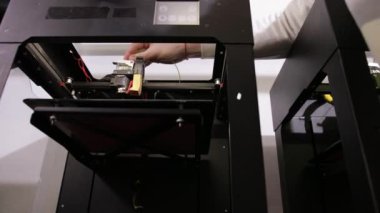 3D technology a young man inserts yellow cable thread into the printer.