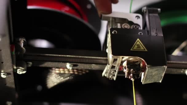 Yellow plastic thread that is printed by 3D printer head hand pushes green cable — Stok video