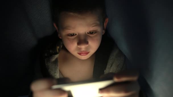 Little guy under the blanket is playing a game on his phone smartphone at night — Stock video